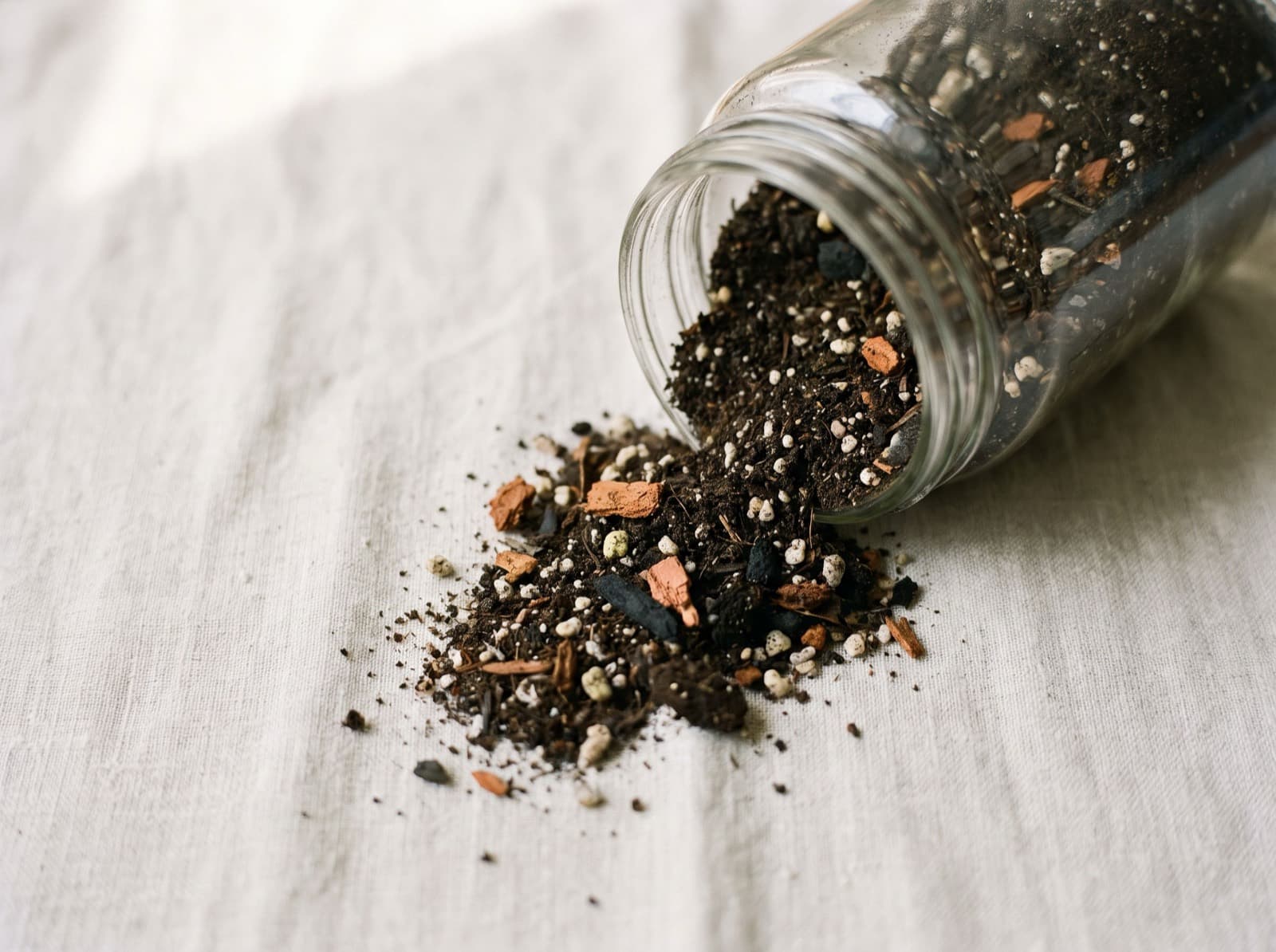 A jar of blended potting mix tipped over, with perlite, bark and compost visible in the spill.